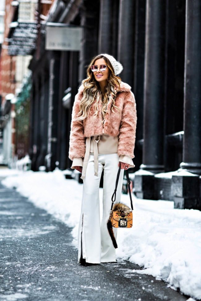 fashion blogger mia mia mine wearing a blush faux fur jacket from asos, white pants from revolve and a furla bag at New york fashion week