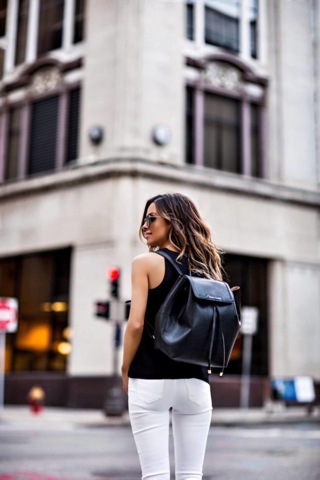 fashion blogger mia mia mine wearing a black armani exchange backpack and white jeans from amazon