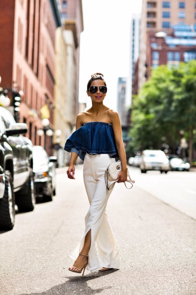 fashion blogger mia mia mine wearing a denim off-the-shoulder top and white pants with stuart weitzman nudesong heels