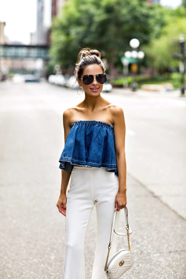 fashion blogger mia mia mine wearing a denim off-the-shoulder top and white high-waisted pants from revolve