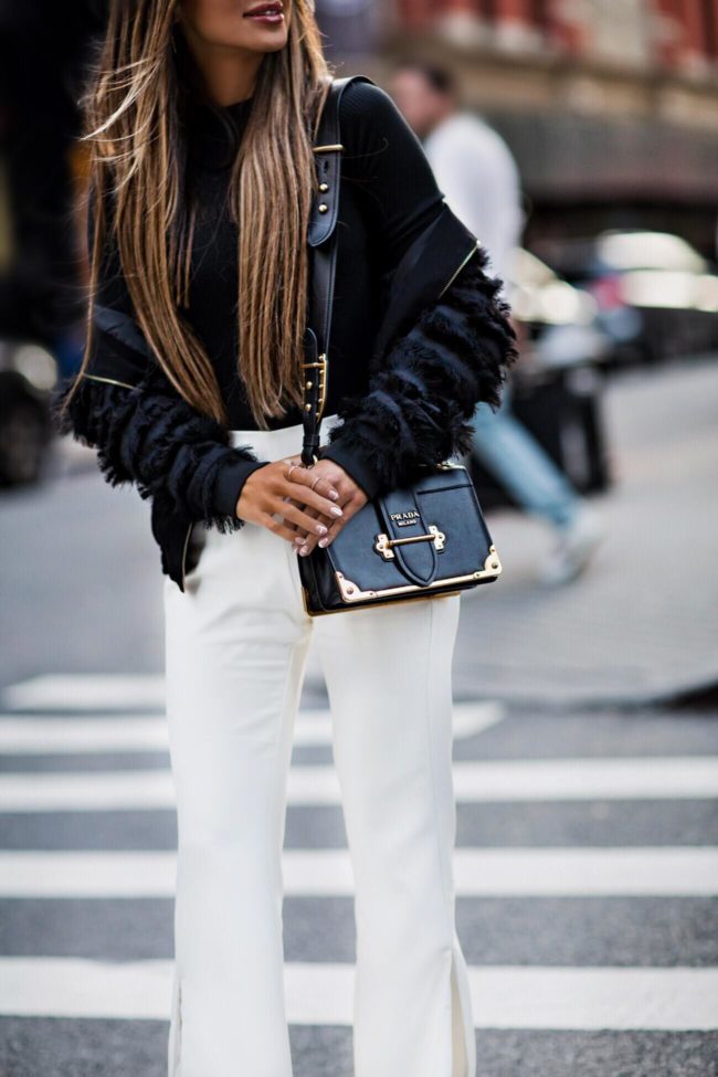 fashion blogger mia mia mine wearing a black fringe bomber jacket from zara and white pants from revolve at nyfw