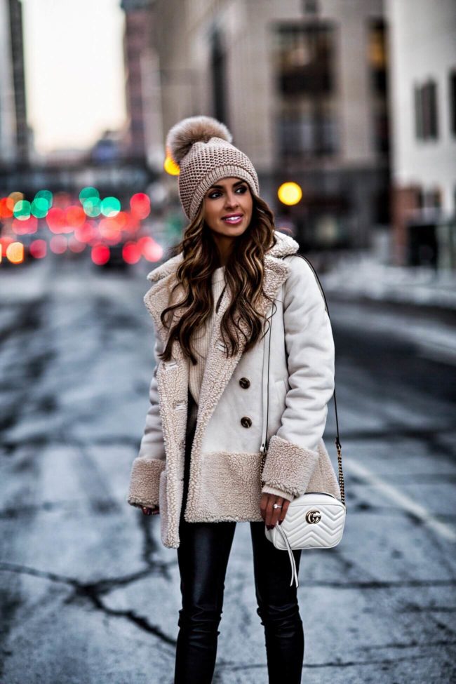 fashion blogger mia mia mine wearing a sherpa jacket and a pom pom beanie from bloomingdales