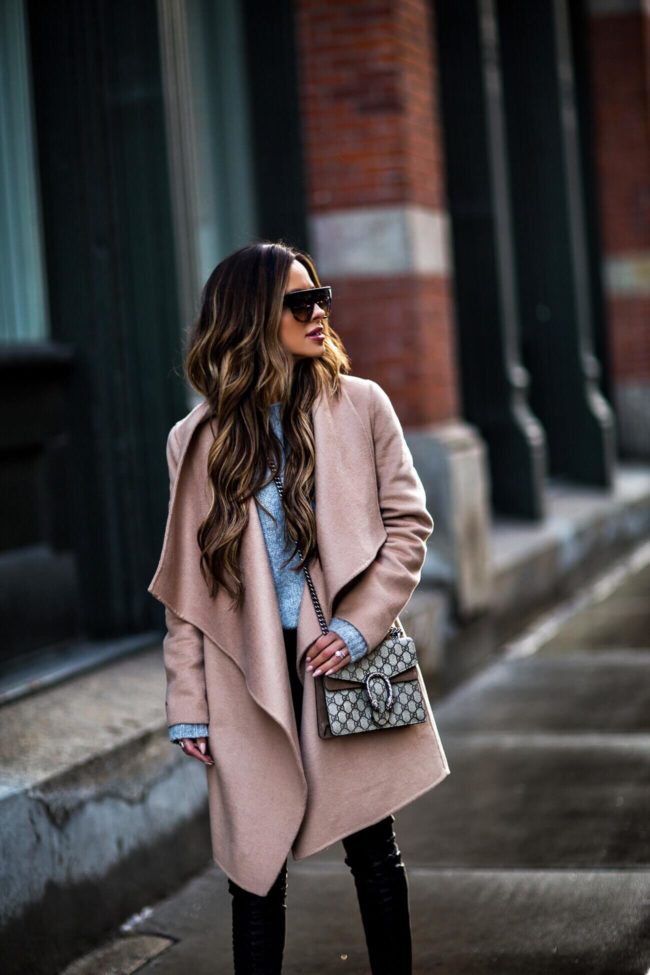 mia mia mine wearing a camel coat and gray sweater