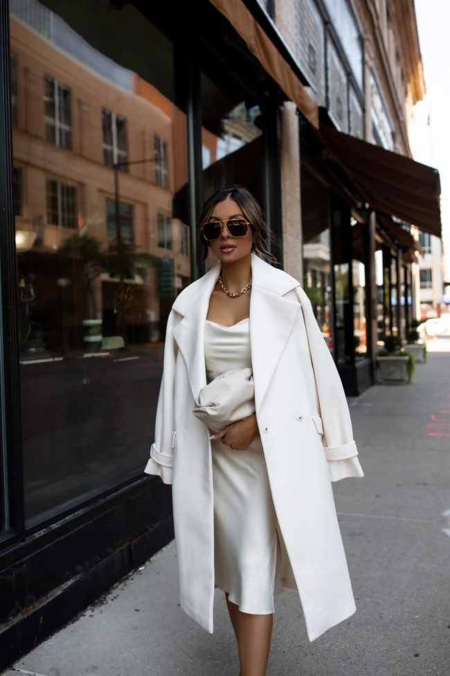 fashion blogger mia mia mine wearing a white silk dress and a white coat from express