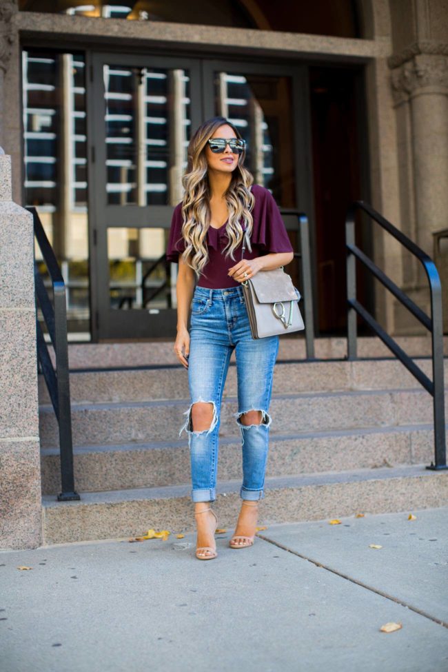 fashion blogger mia mia mine wearing a burgundy cape bodysuit from nordstrom and levis jeans
