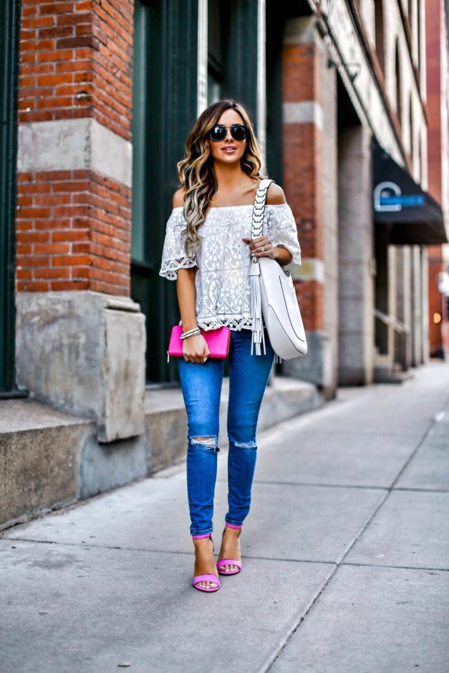 fashion blogger mia mia mine wearing a white lace off-the-shoulder top and a bright pink wallet from henri bendel
