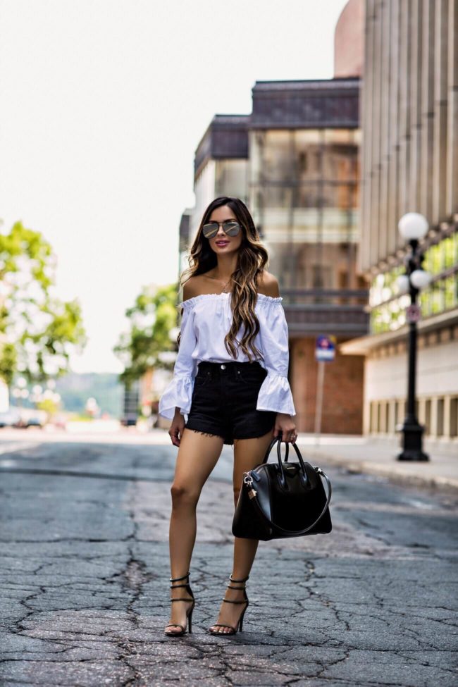 fashion blogger mia mia mine wearing a white bell sleeve top and black denim shorts by frame