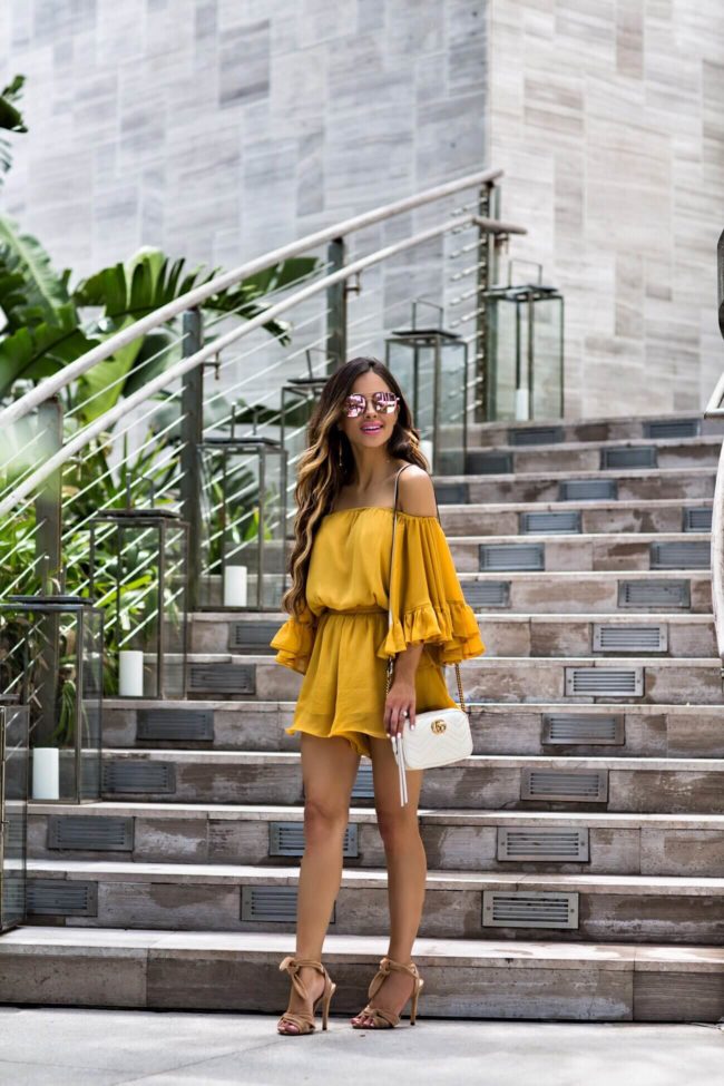 fashion blogger mia mia mine wearing a yellow off the shoulder romper from revolve, quay mirrored sunglasses and nude heels by schutz