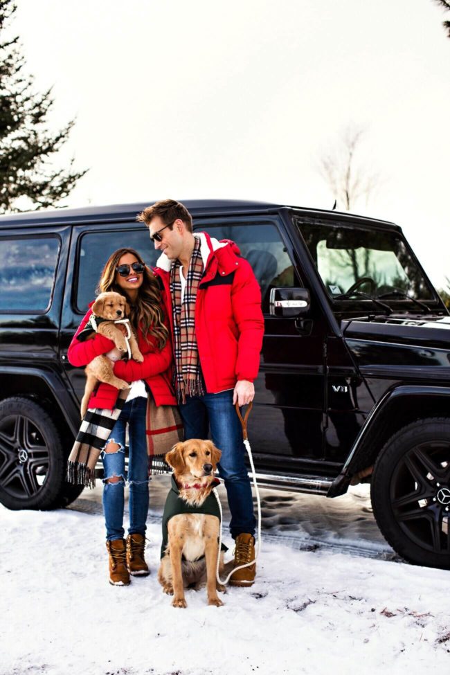 fashion blogger mia mia mine wearing a red puffer coat with husband and dogs at a tree farm