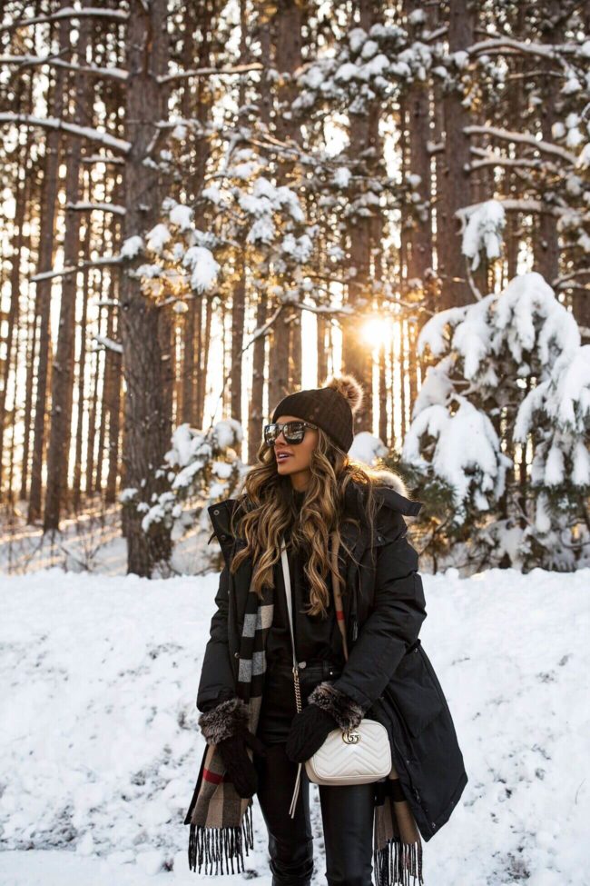 fashion blogger mia mia mine wearing a winter outfit in a snowy forest