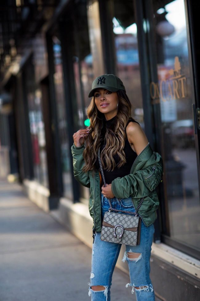 fashion blogger mia mia mine wearing an olive bomber jacket by alpha industries and a ny cap