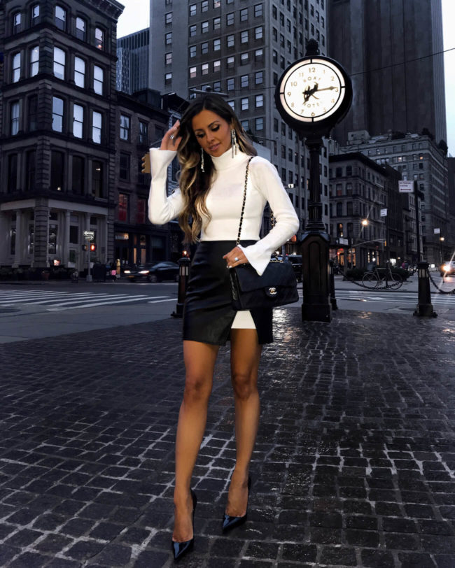 fashion blogger mia mia mine wearing a white sweater dress from revolve and a faux leather skirt