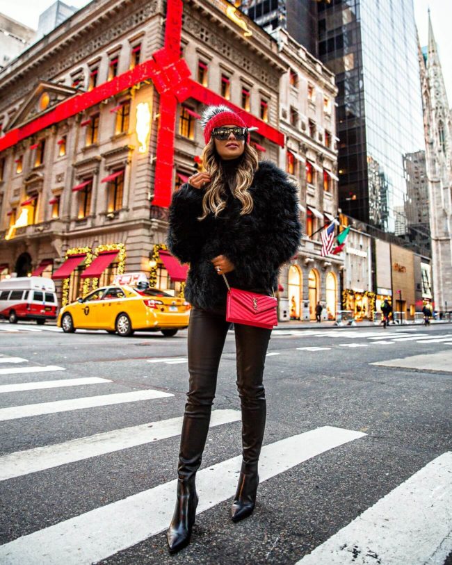 fashion blogger mia mia mine wearing a red beanie hat and feather jacket with faux leather pants
