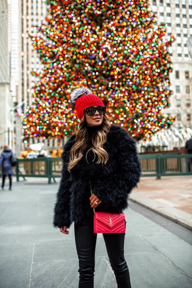 fashion blogger mia mia mine wearing a feather jacket and a red beanie hat for winter in NYC