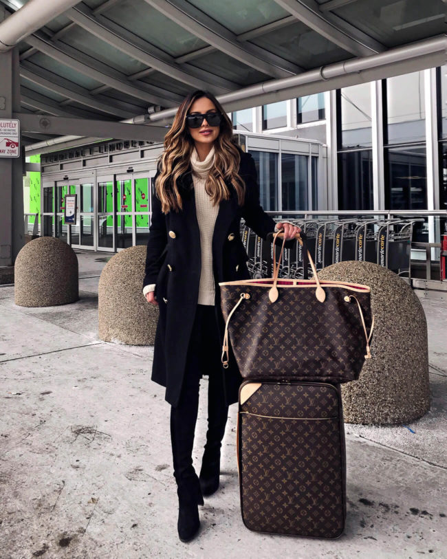 fashion blogger mia mia mine wearing a black coat and louis vuitton luggage to travel