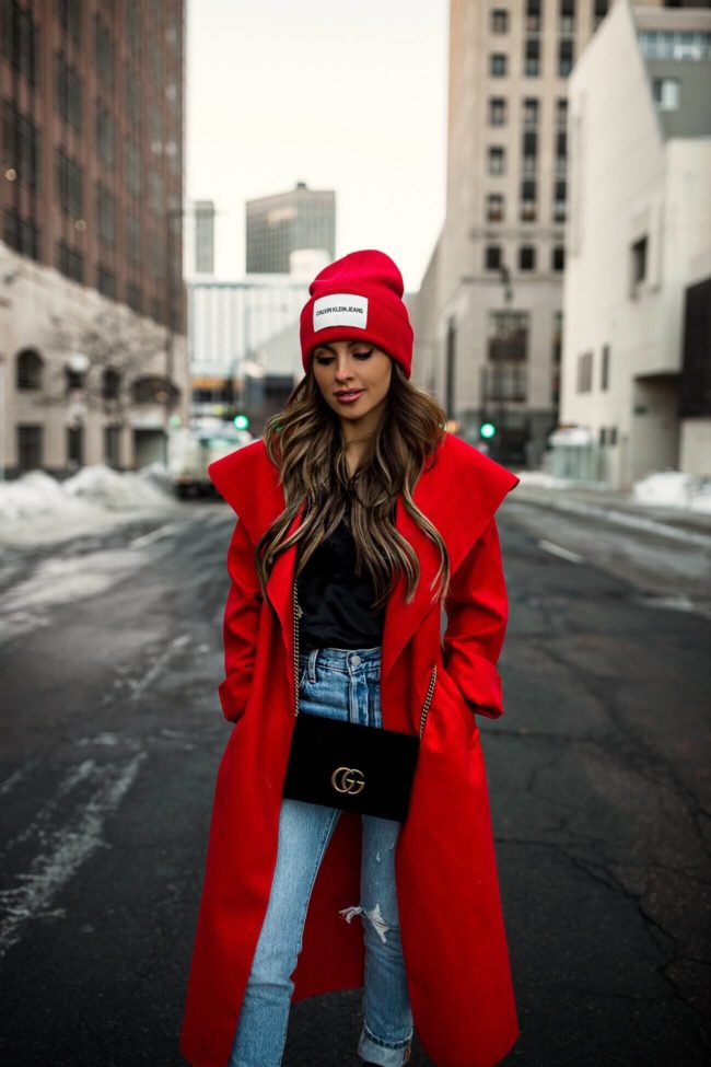 fashion blogger mia mia mine wearing a red duster coat and a calvin klein beanie