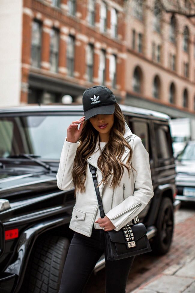 fashion blogger mia mia mine wearing an adidas hat and a white leather jacket for spring