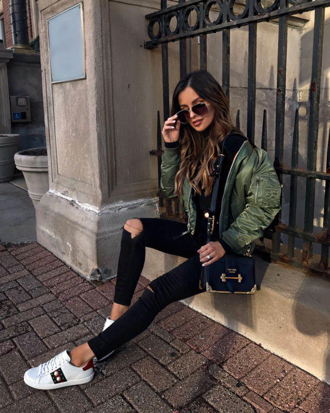 fashion blogger mia mia mine wearing gucci sneakers and an olive bomber jacket with a prada cahier bag