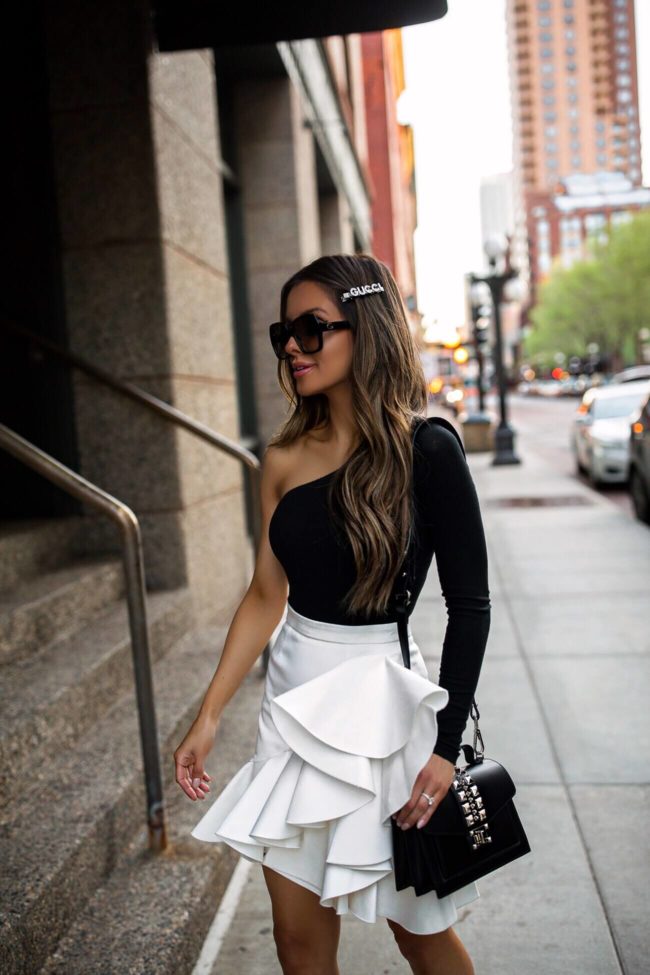 fashion blogger mia mia mine wearing a one shoulder black bodysuit and a white ruffle skirt with a valentino bag