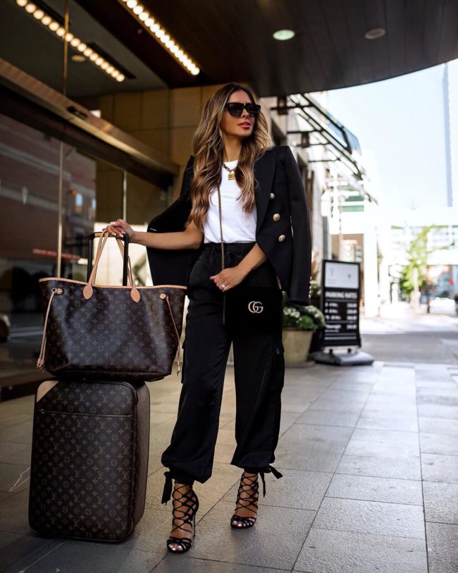fashion blogger mia mia mine wearing black jogger pants and lace-up heels with louis vuitton luggage