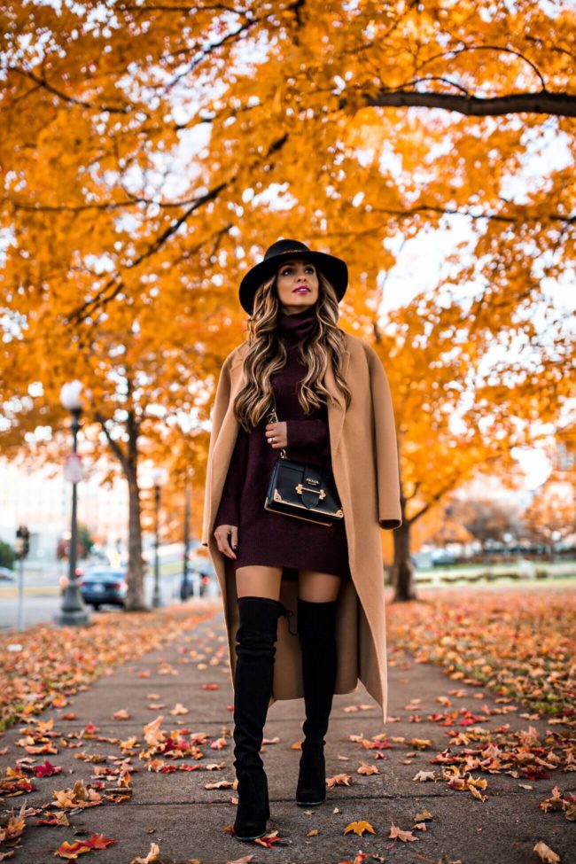fashion blogger mia mia mine wearing a burgundy sweater dress with a camel coat and over-the-knee boots from Stuart Weitzman