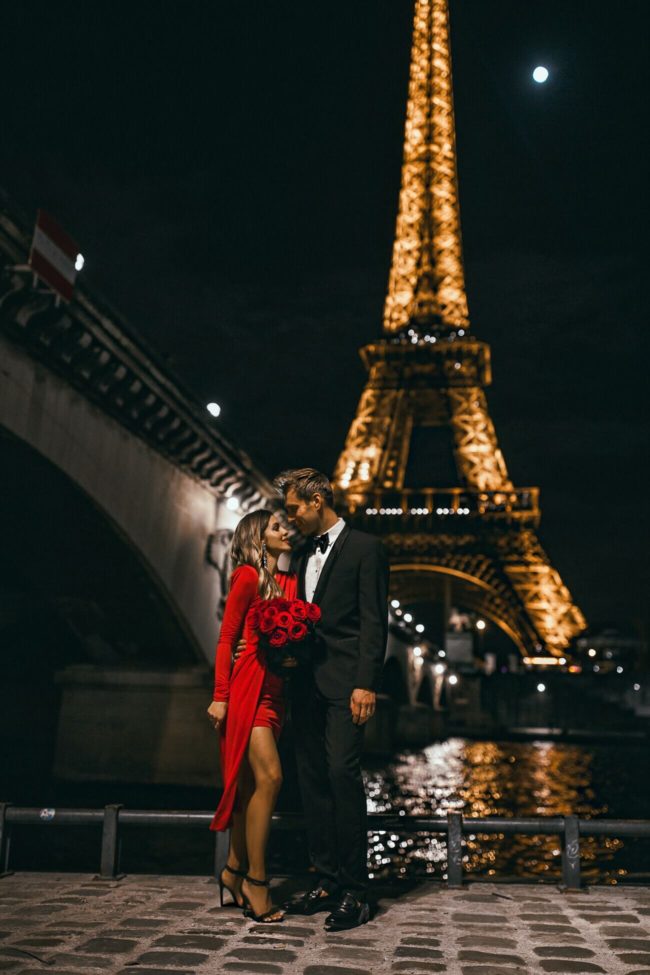 fashion blogger mia mia mine wearing a red dress with husband in front of the eiffel tower in paris