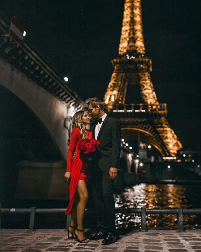 fashion blogger mia mia mine wearing a red dress with husband in front of the eiffel tower in paris