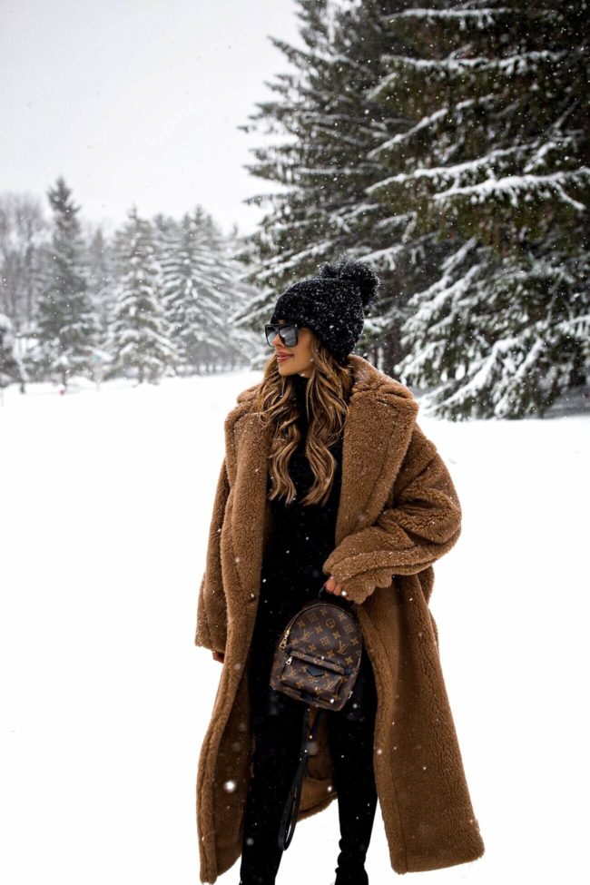 fashion blogger mia mia mine wearing a max mara coat and a louis vuitton palm springs mini backpack in the snow