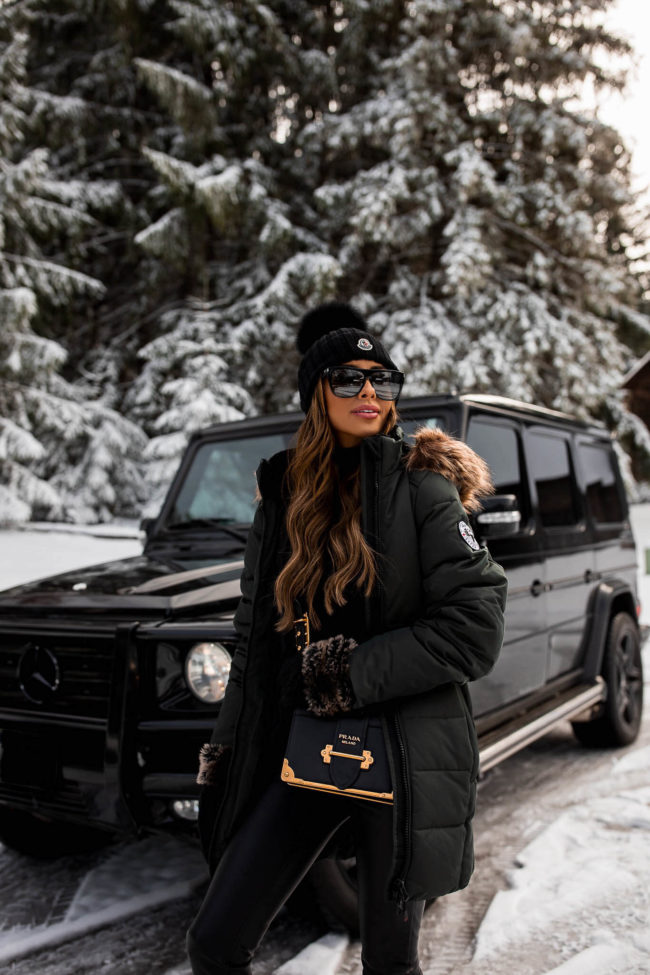 fashion blogger mia mia mine wearing an all black outfit with a green parka for winter