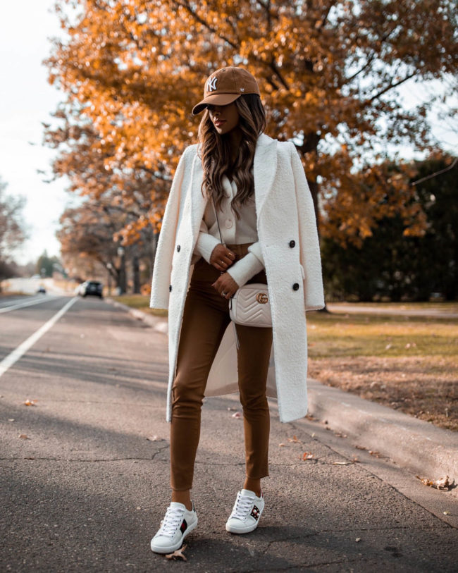 fashion blogger mia mia mine wearing a white coat from express with tan coated jeans and gucci ace sneakers