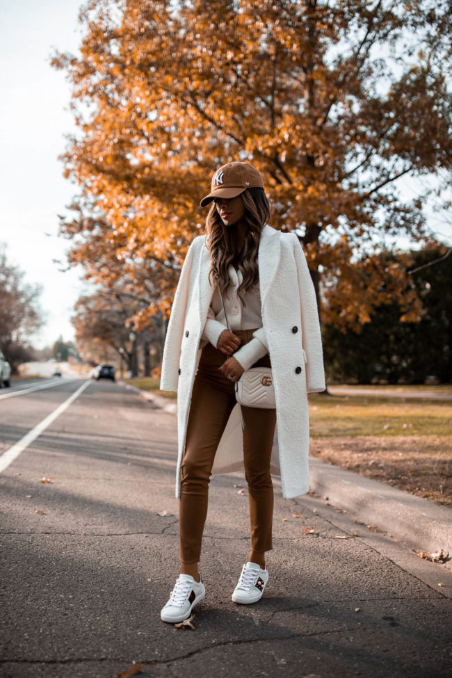 fashion blogger mia mia mine wearing a white coat from express with a cardigan and ny yankees baseball cap