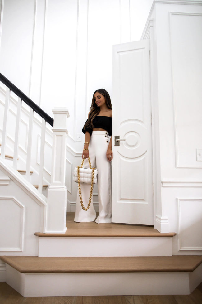 fashion blogger mia mia mine wearing white trousers and a black top in her entryway