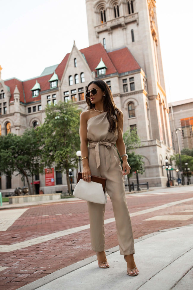 fashion blogger mia mia mine wearing a one shoulder tan jumpsuit from express