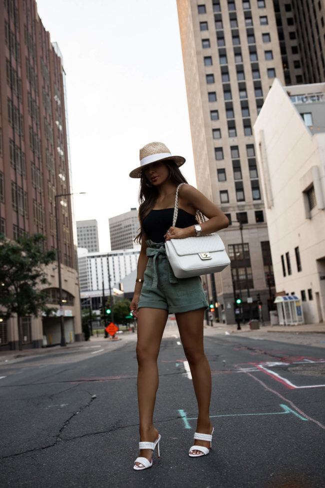 fashion blogger mia mia mine wearing a black bodysuit and green paperbag waist shorts from saks off 5th