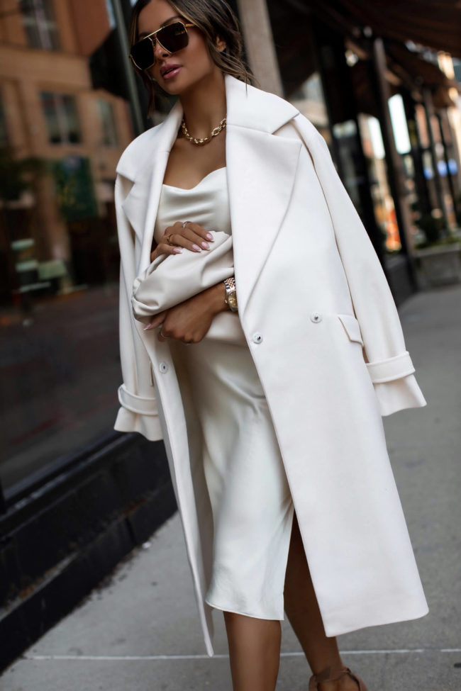 fashion blogger mia mia mine wearing a white coat and white satin dress from express