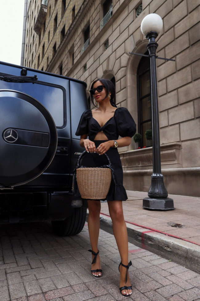 fashion blogger mia mia mine wearing a saint laurent straw bag and a black summer dress from saks