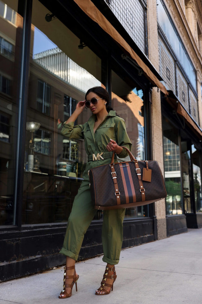 fashion blogger mia mia mine wearing a green utility jumpsuit and michael kors heels