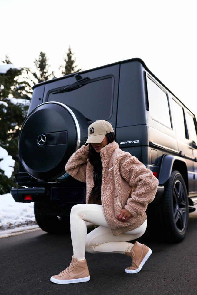 fashion blogger mia mia mine wearing a white one piece jumpsuit and a tan sherpa nike jacket from nordstrom