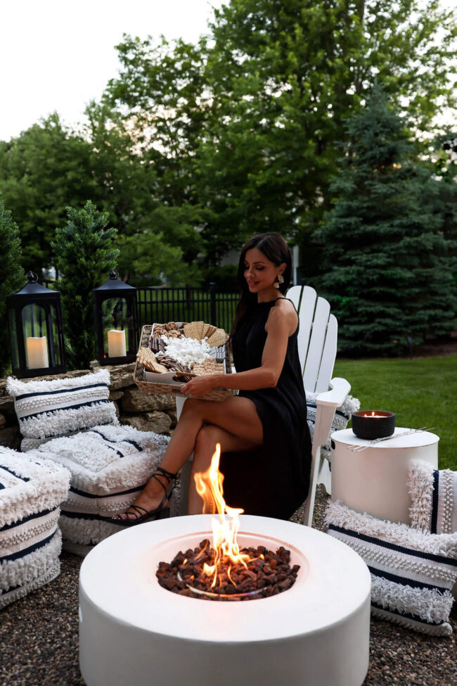 brunette woman sitting by a fire in her backyard