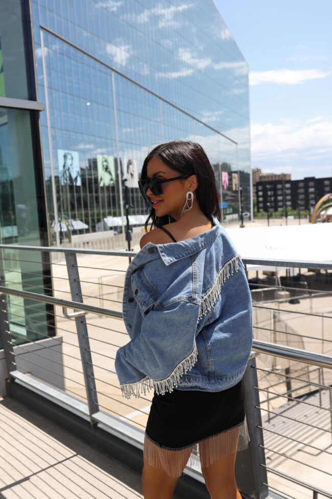 fashion blogger wearing a denim jacket with crystal fringe trim for a summer concert