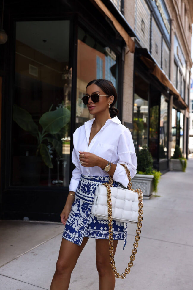 fashion blogger mia mia mine wearing a blue and white skirt and a white bottege veneta bag from saks
